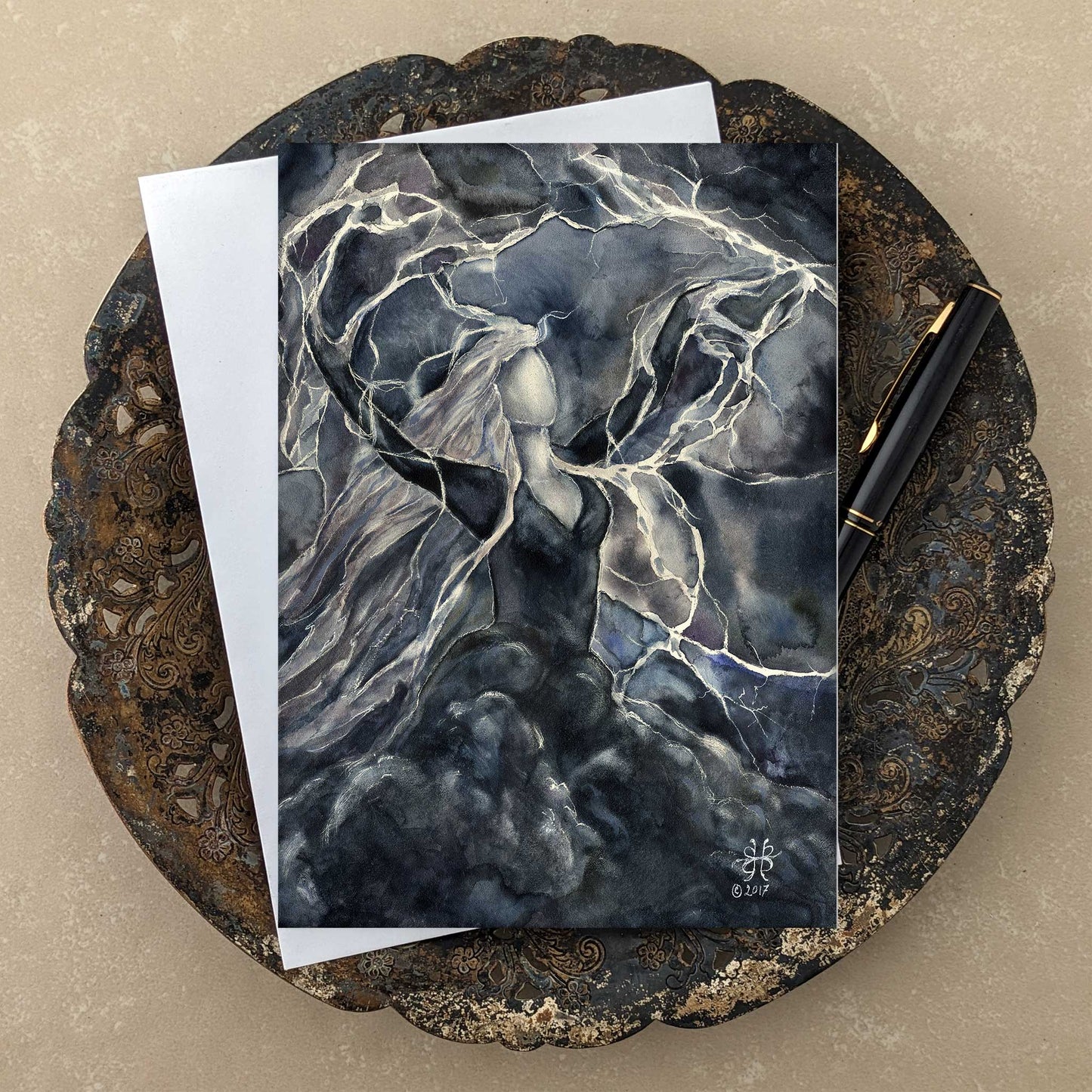 Storm Goddess art greeting card with lightning and rolling black clouds  a white envelope and black and gold pen on tarnished antique tray